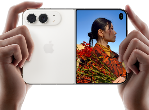 iPhone Duo, สีสตาร์ไวท์, ถืออยู่ในมือสองข้างในแนวนอน, กางเปิดอยู่, แผงด้านซ้ายแสดงกล้องหลัง Dual Fusion 48MP, แผงด้านขวาแสดงบุคคลหนึ่งขณะถ่ายภาพบนจอภาพภายนอก, ตัวแบบในภาพสามารถเห็นใบหน้าของตัวเองระหว่างกำลังถ่ายภาพโดยใช้ Duo Preview